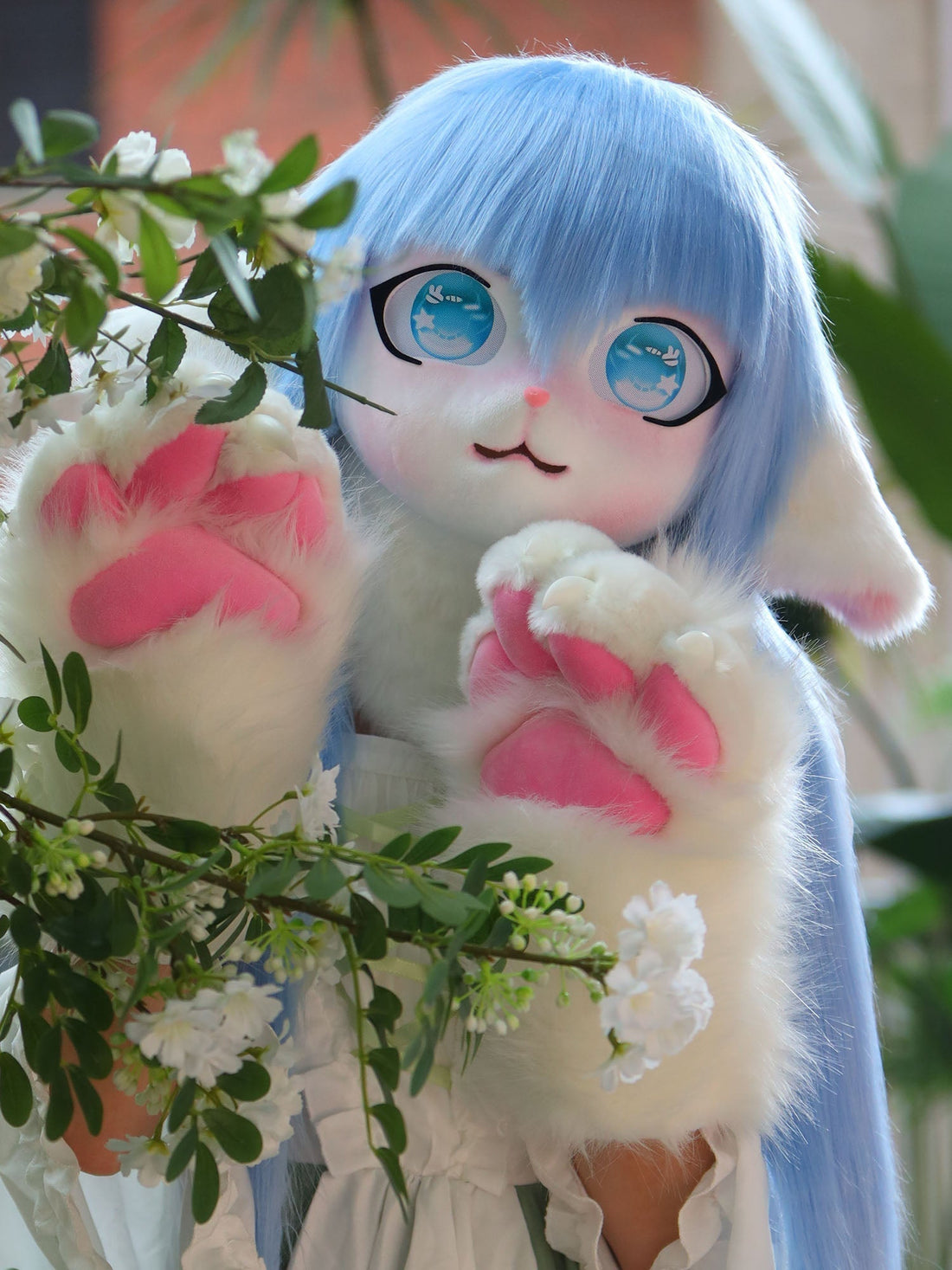 Blue-haired anime mascot costume with big blue eyes and furry paws by flower bushes