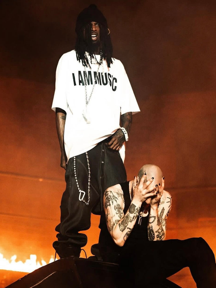 Urban streetwear scene with two men, one in 'I AM MUSIC' shirt, tattoos, bold accessories, fiery background